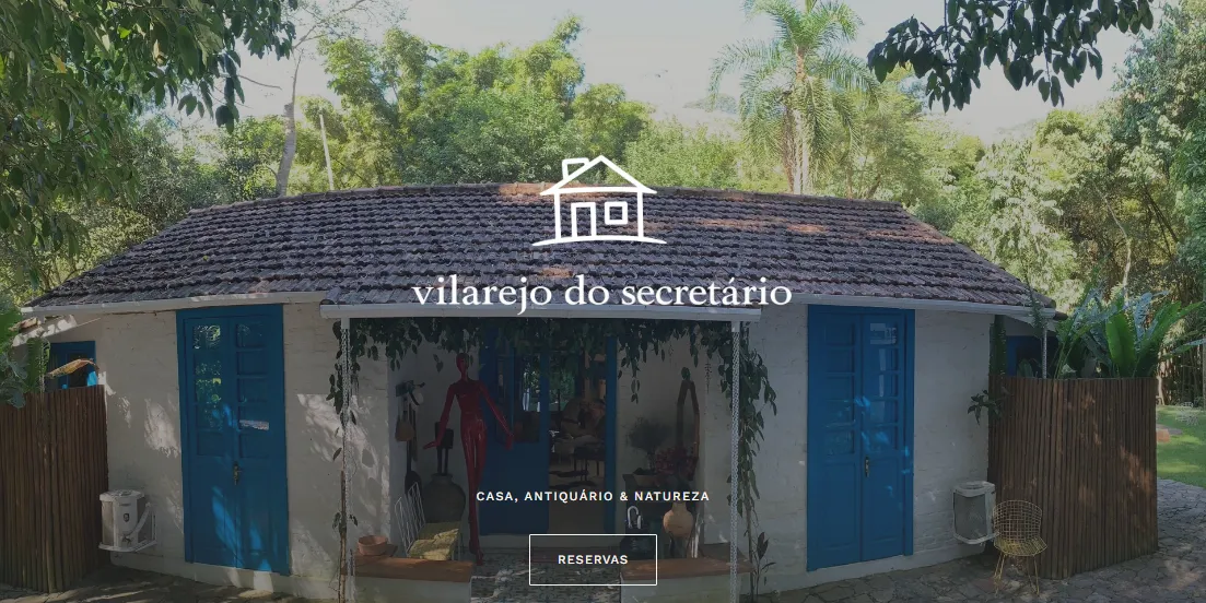Página inicial do site do Vilarejo do Secretário, com a logomarca sobre a fachada de portas azuis.