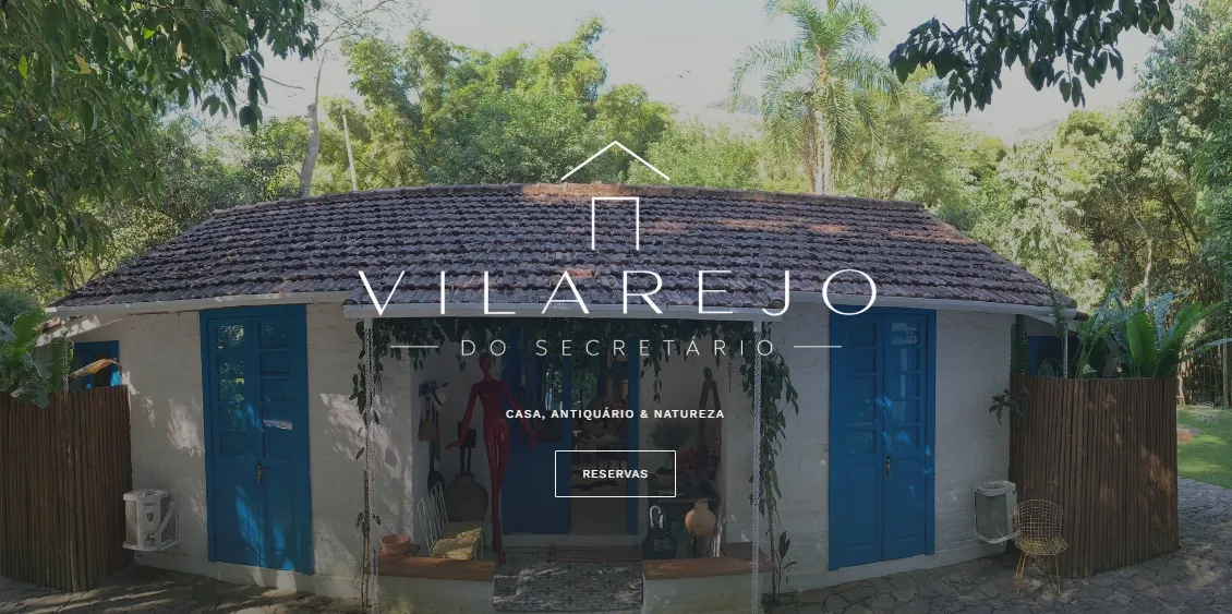 Página inicial do site do Vilarejo do Secretário, com a logomarca sobre a fachada de portas azuis.